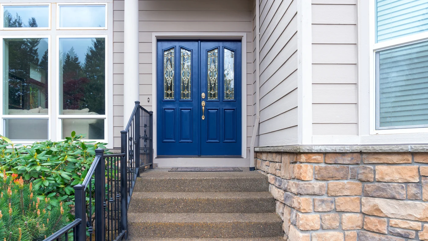 A blue door with detailed glass panes in a home with gray siding