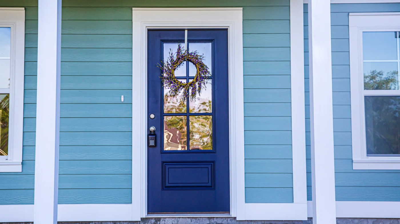 Blue entry door with wreath against door with light blue siding and white trim