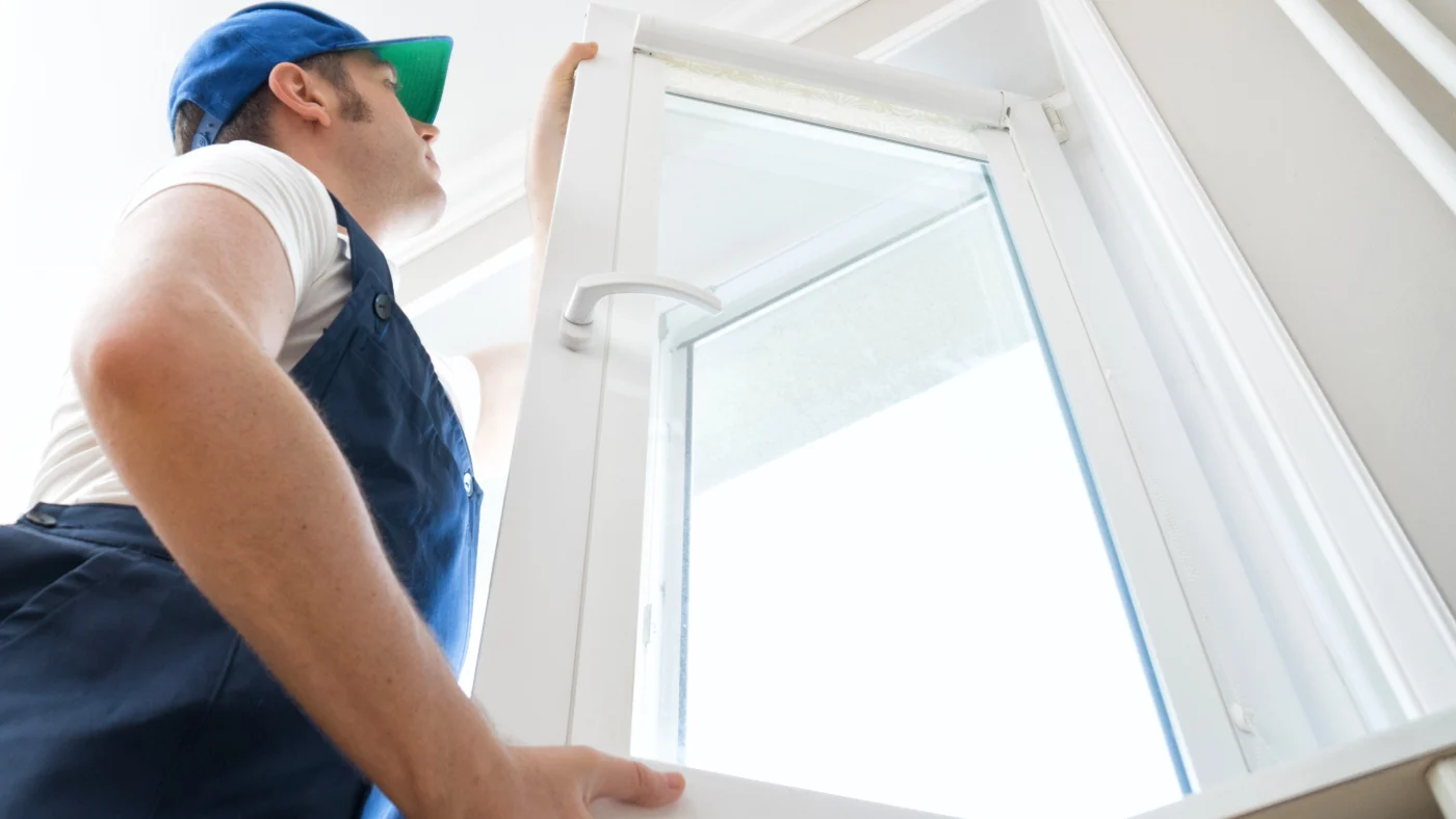 A handyman is installing a white window in a home