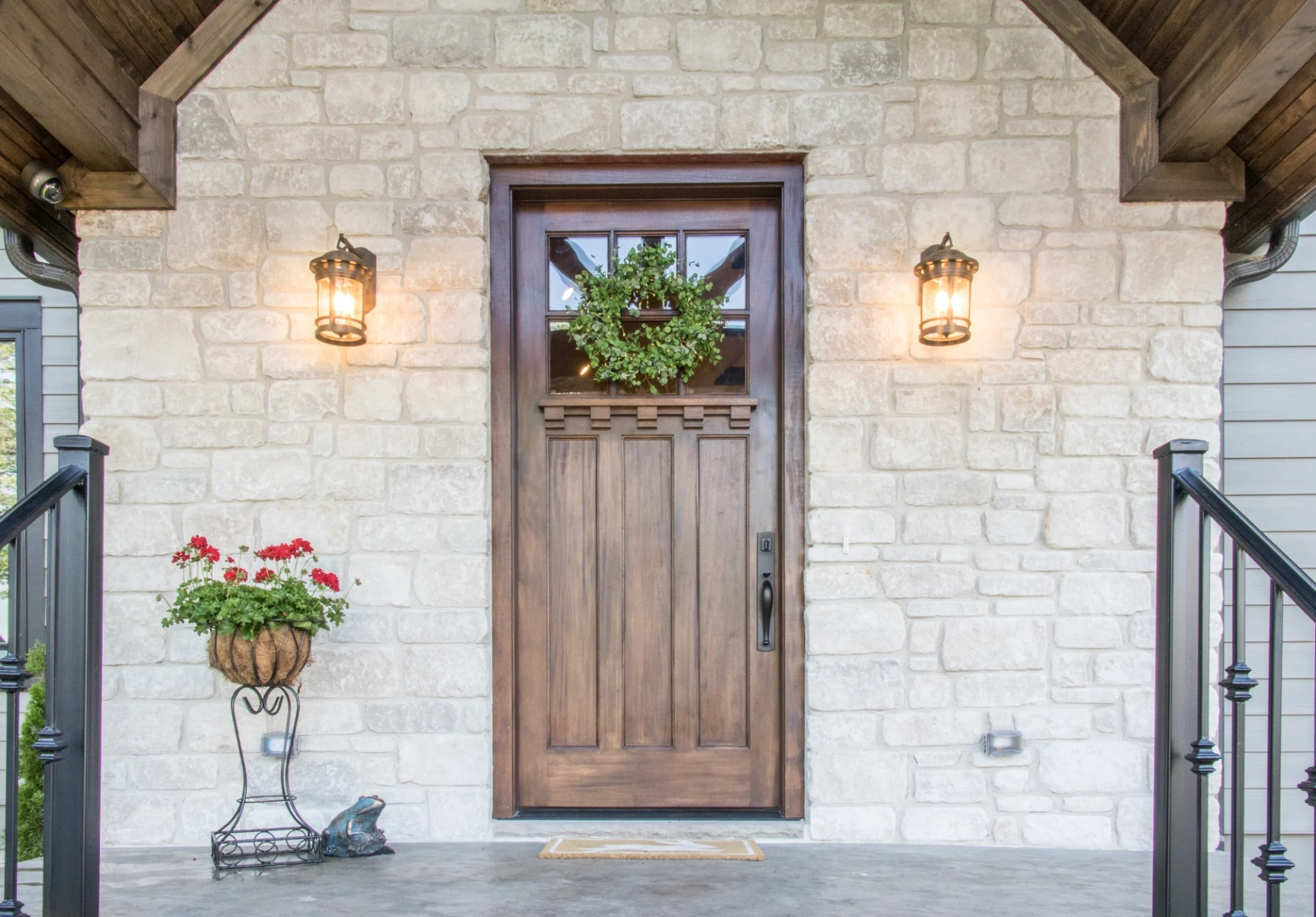 There is a dark wood front door with a window on a stone entrance into the home