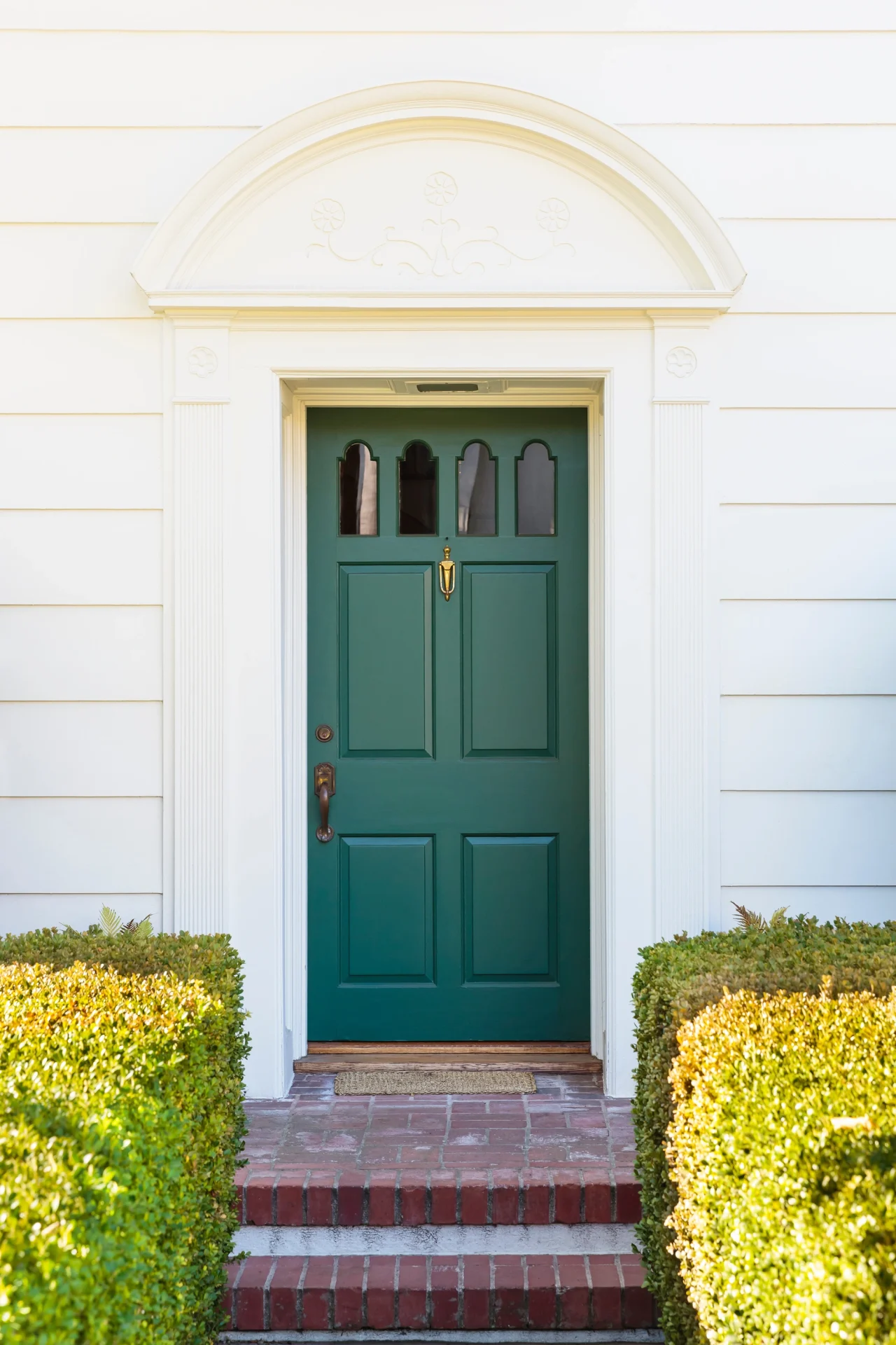 A beautiful entry door in a dark blue-green color with multiple small arched glass inserts