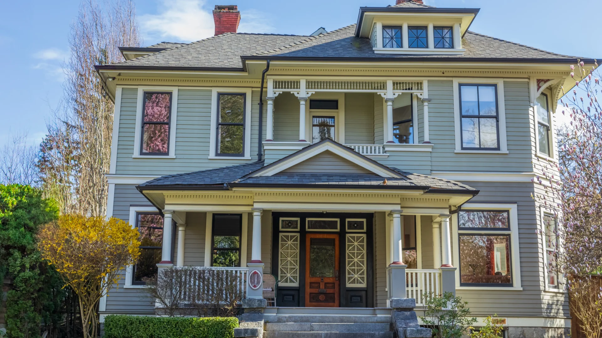 Large luxury Victorian-style home with green and gray siding and lots of windows with black frames