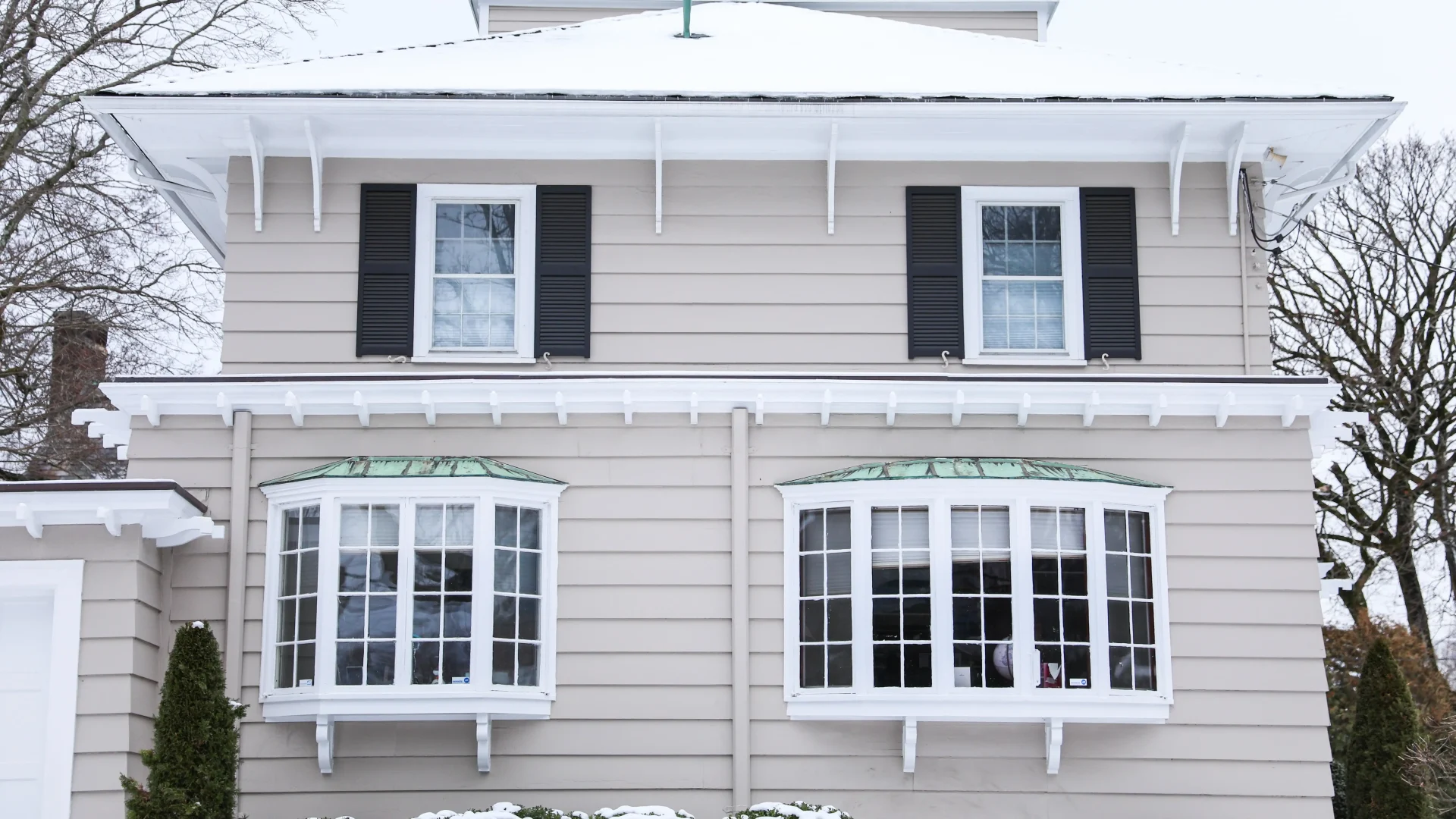 Home exterior in the winter with brown siding and windows with white frames and dark shutters