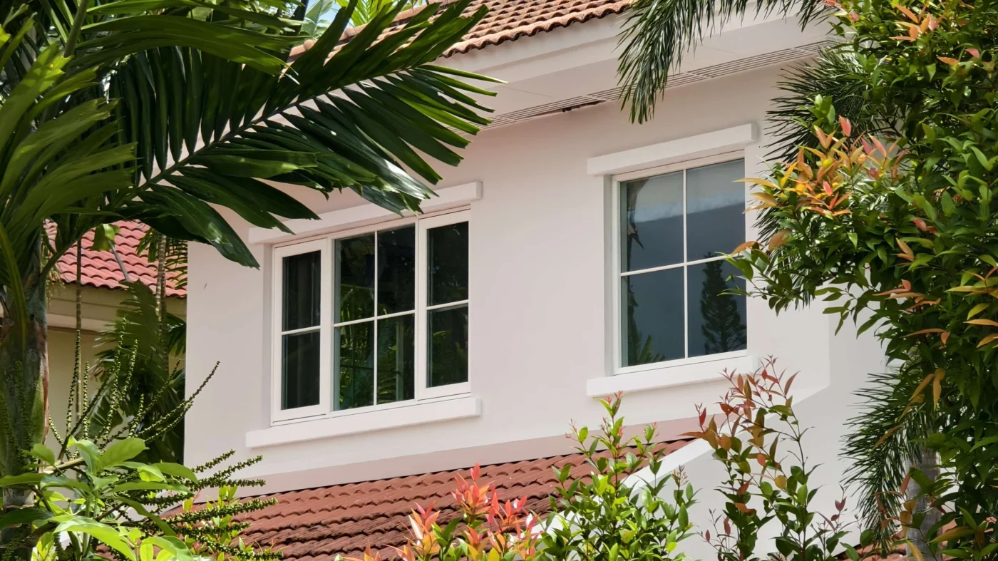 Exterior view of windows in upper level of house, with tropical foliage in foreground