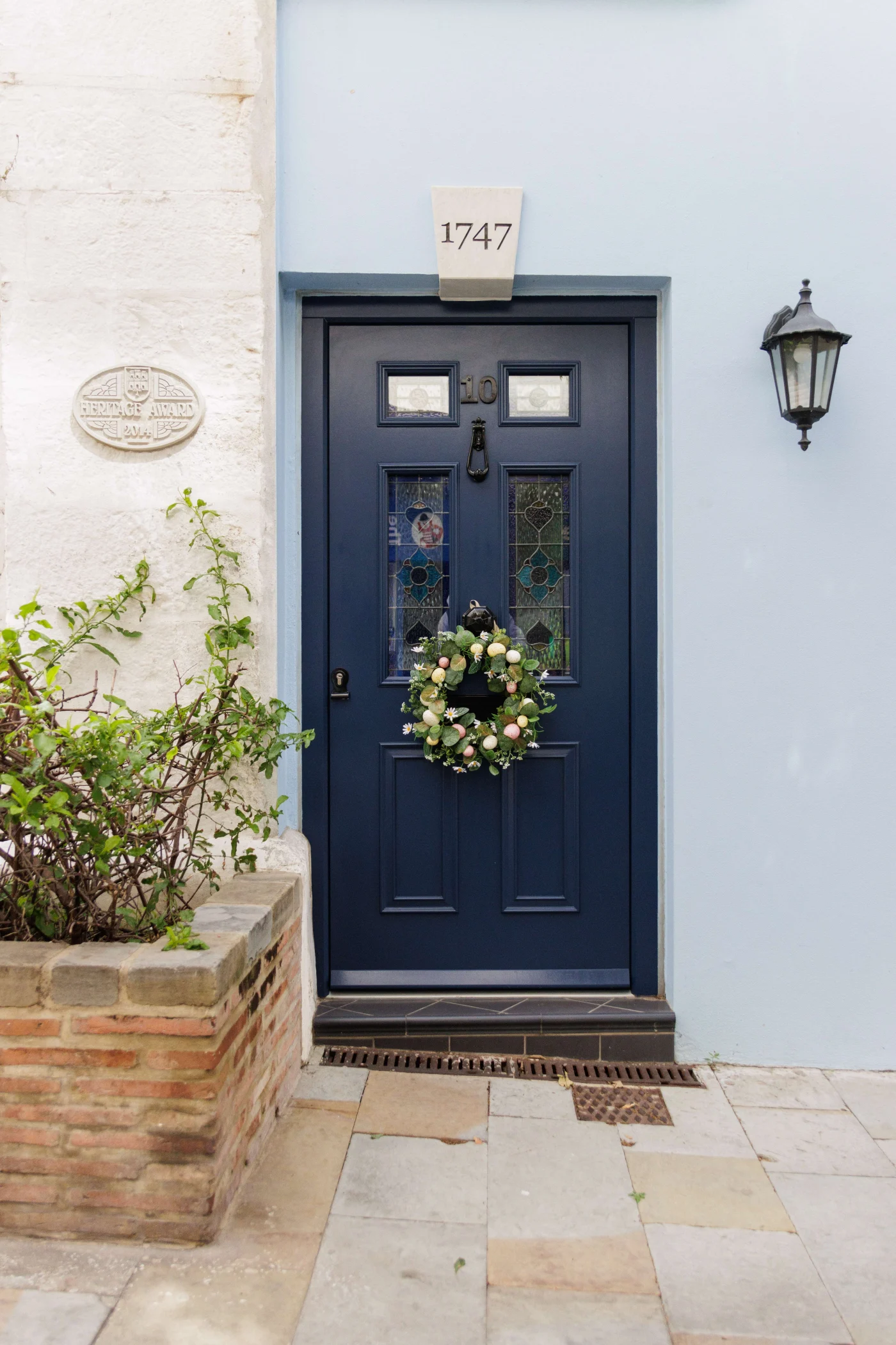 A Blue Door With A Wreath On It And The Number 1747 On It An image of a young, bearded man looking out of a large, white, wooden, 12-pane, classic, double-hung, sash window with a blue shutter