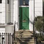 An image of an inviting, bright green, vintage-inspired wood front entry door replacement on the top of front entry steps on a white home with an old-fashioned mail slot