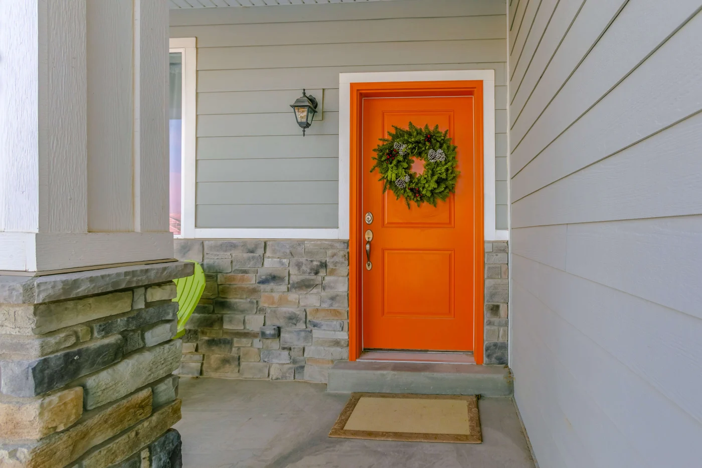 An orange front door on a gray house with a stone base