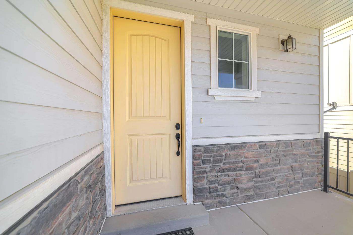 A yellow front door with a black handle and lock on a house with a stone base and a porch