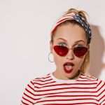 A young woman with sunglasses, make-up, and clothing patterned with the American flag, looking surprised.