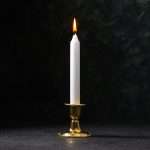 A tall white candle in a bronze candleholder with a flame against a textured black background.